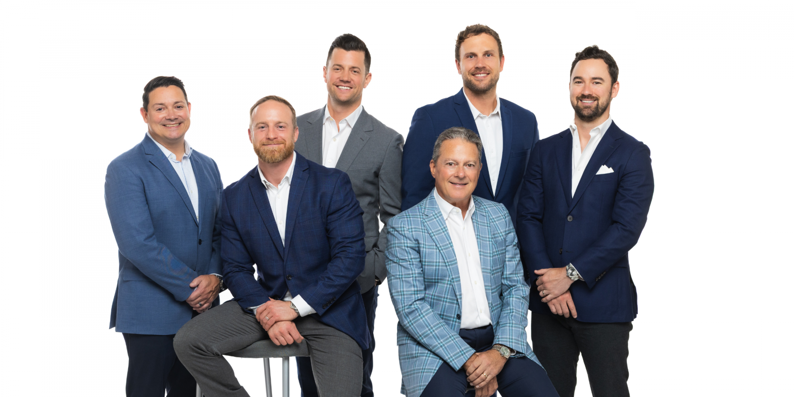Six adults in professional business attire stand together, smiling, against a plain white background in a black-and-white photo.